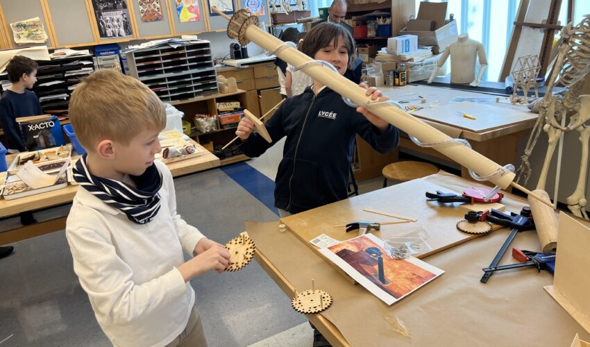 Fourth graders work at an art table to rebuild on of Leonardo Da Vinci's inventions.