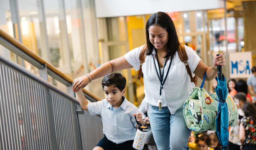 Mother and son walk up a staircase of a school to head to a classroom.