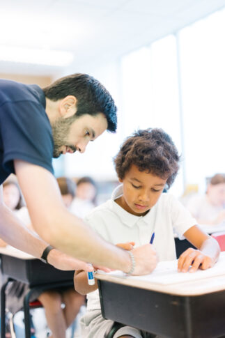 Teacher guides a student at his desk in the elementary school.