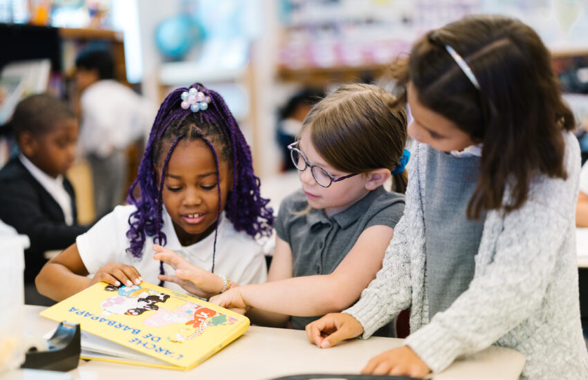 Three Elementary school students sit at a table and read a French children's book